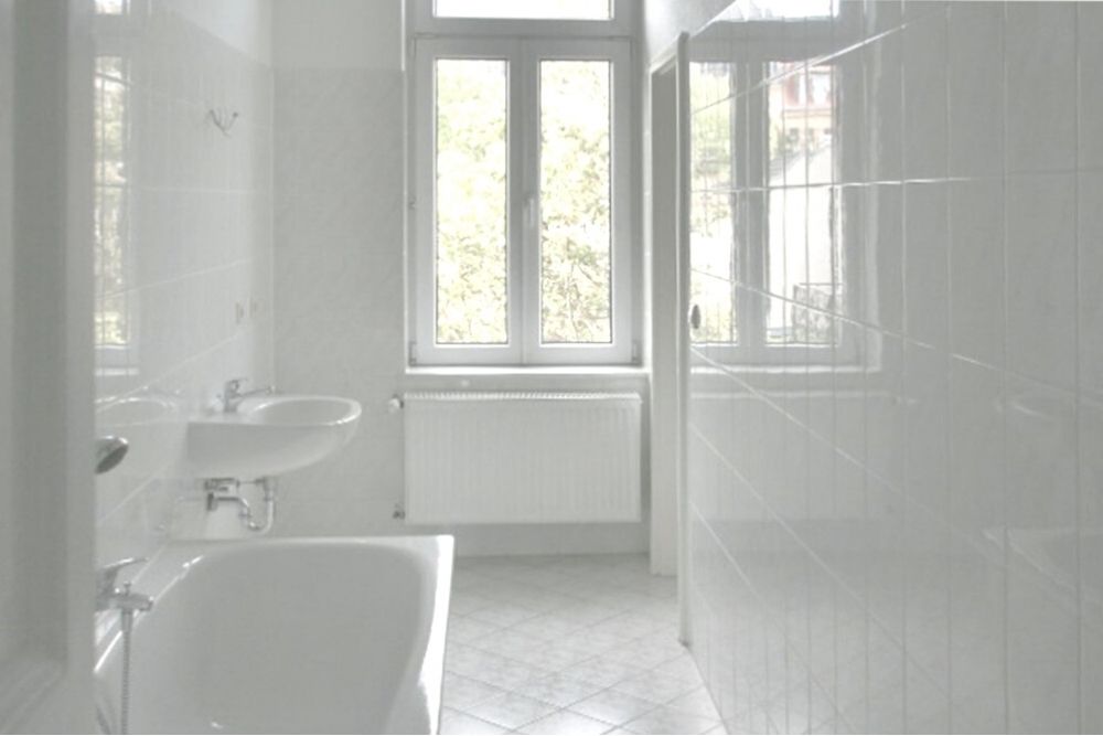 Ein leeren Badezimmer, ganz in weiß gefliest. Die Fliesen sind langweilig und haben banale Muster, obendrein unterschiedliche.