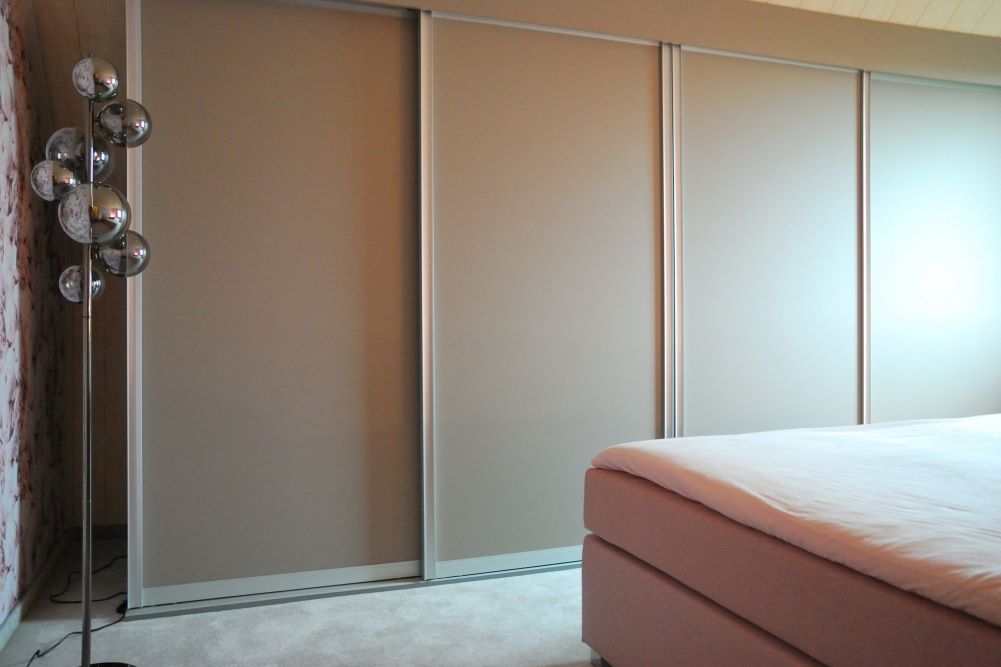 Romantisches Schlafzimmer gestalten, Detailaufnahme: Ein rosa Boxspringbett, ein Schiebetürenschrank in Grau- bzw. Rosenholz-Tönen und ein flauschiger Teppich in exakt der Farbe der Schiebetüren.