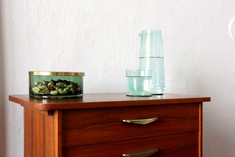 Kleines Zimmer als Büro einrichten, Detail: Ein kleines Schränkchen aus Teak mit Rauchglaskaraffe für Wasser und einer Schale für Kanbbereien.