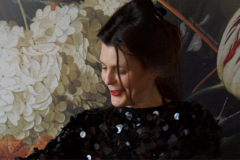 Diana Kuba vor tollen Wandbild aus bunten Blumen auf schwarzem Untergrund.