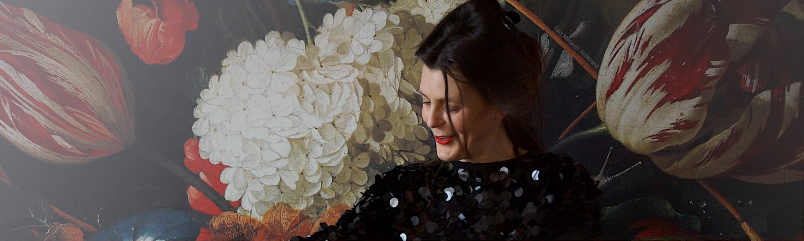 Porträt Diana Kuba vor tollen Wandbild aus bunten Blumen auf schwarzem Untergrund.