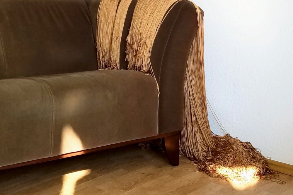 Ein braunes Sofa, über der Sofalehne hängen lange goldene Fäden zum Entwirren.