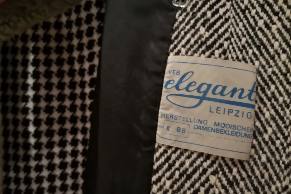 Garderobeninhalt Detail: ein Mantel mit Etikett VEB Elegant Leipzig.