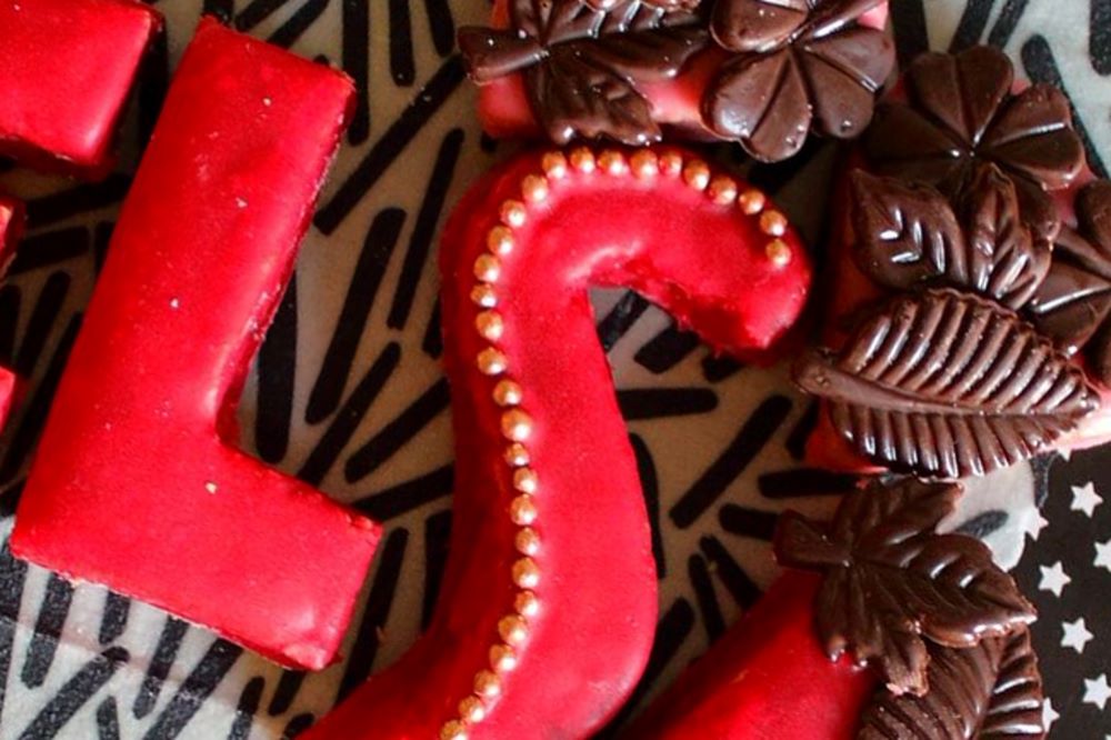 Mürbeteig-Buchstaben mit rotem Zuckerguss, goldenen Perlen und Schokoladenblättern.