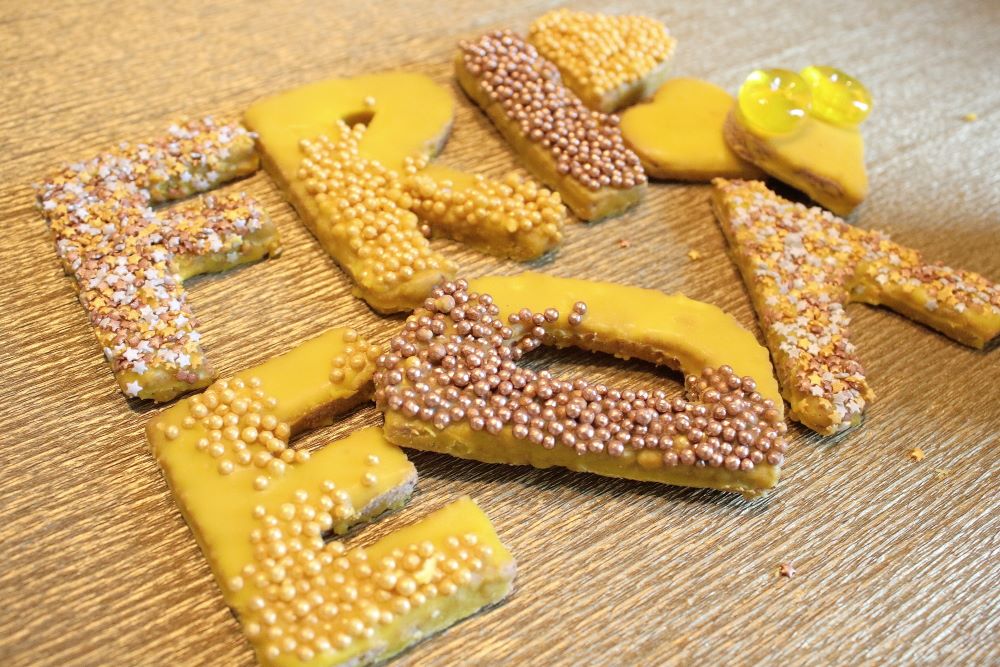 Mürbeteig-Buchstaben mit gelbem Zuckerguss und Verzierungen in bronze, silber, gelb. Und mit Gummitieren.
