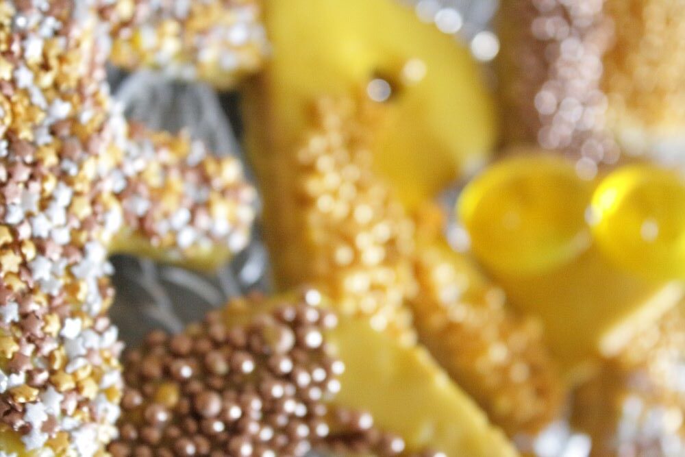 Buchstaben-Plätzchen mit gelbem Zuckerguss und Sternchen und Kugeln aus bronze und silber.