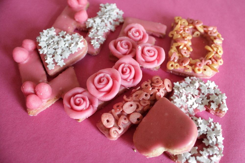 Mürbeteig-Buchstaben mit rosa Zuckerguss und rosa und silbernen Verzierungen.