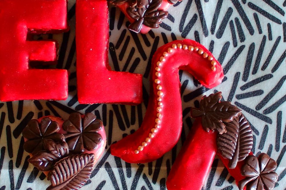 Vier Buchstaben aus Mürbeteig mit rotem Zuckerguss und Schokoladenblättern ergeben den Namen Elsa. Plätzchen zur Schuleinführung als Zuckertütenbeigabe.