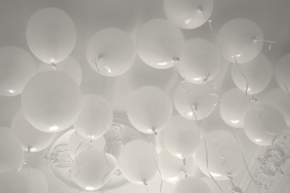 Weiße Luftballons schweben an einer weißen Zimmerdecke.