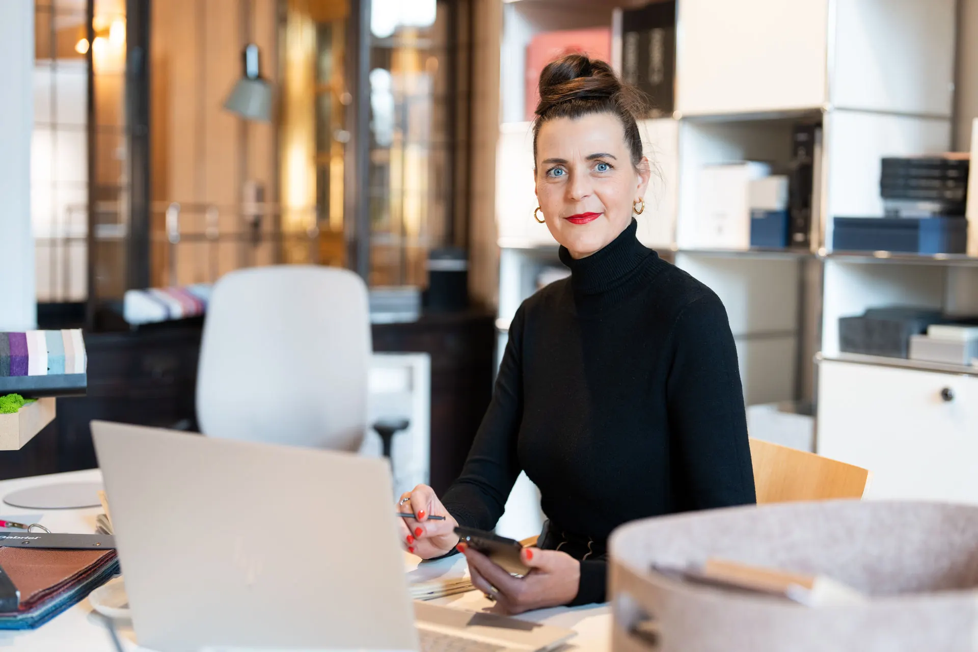 Eine Frau sitzt in einem modernen Büro am Schreibtisch und lernt neue Kunden für ihr Interior Design Leipzig kennen.