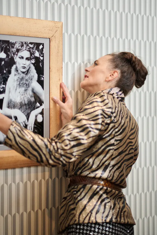 Eine Frau hängt ein gerahmtes Schwarz-Weiß-Foto von Kate Moss an eine Wand mit Mustertapete.